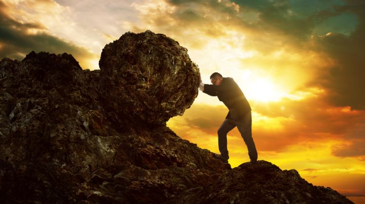 A man struggling to push a boulder up a hill. 