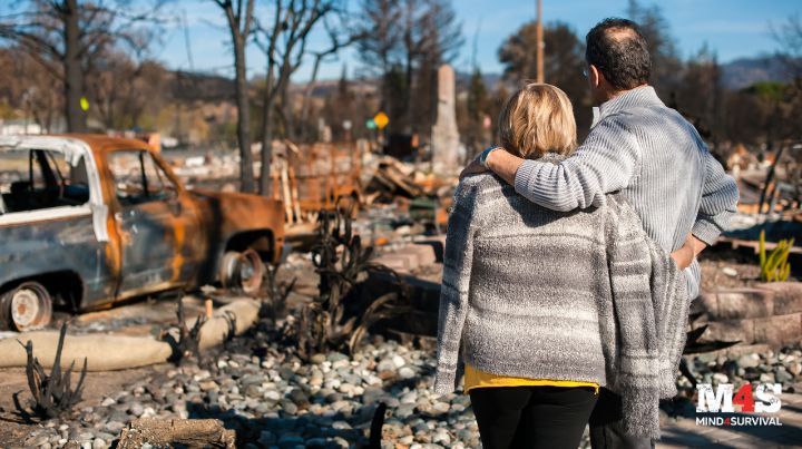 A man and woman looking at their home that is burned down from a wildfire.